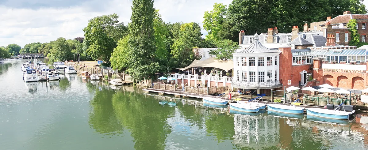 The River Thames at Hampton Court with boats on the water, and buildings and trees lining the riverside.