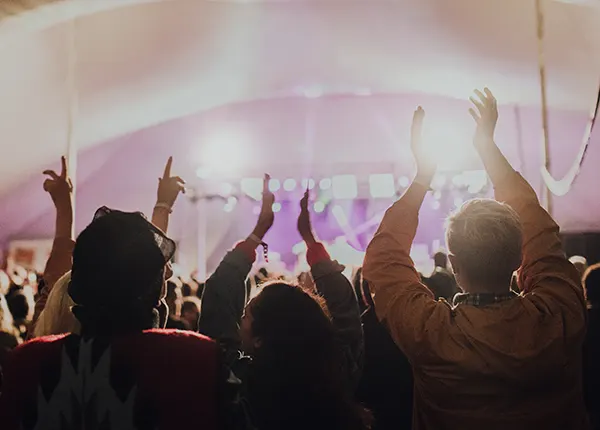 A crowd of festival-goers with hands raised inside a large tent, bathed in warm and purple stage lighting.