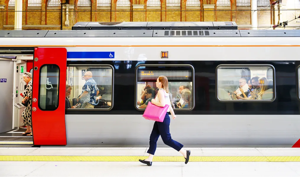 Person with pink bag rushing past train at historic station with ornate yellow brick arches and vaulted ceiling.