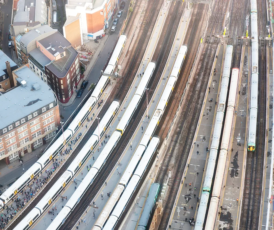 Aerial view of a busy station with multiple tracks, there are trains at many of the platforms and groups of passengers standing.