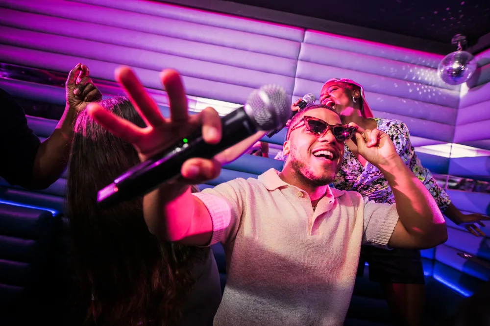A Black man in a karaoke booth, wearing sunglasses and holding a microphone. 