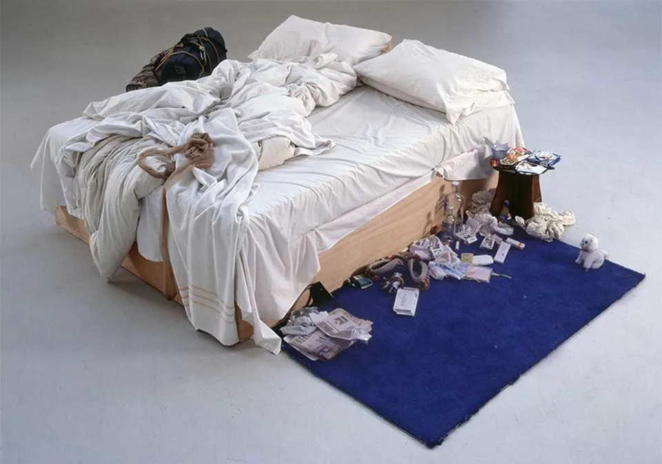 Artwork by Tracy Erin – an unmade bed with rumpled white sheets on wooden frame, surrounded by clutter on a blue rug.