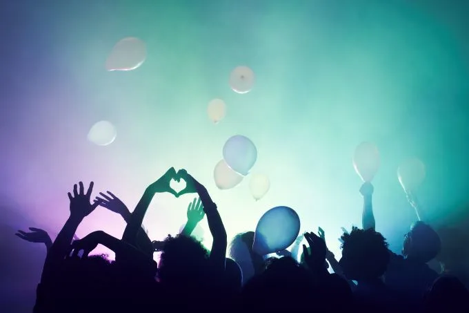 Silhouettes of hands in the air enjoying a concert, looking on at colourful lights and balloons in the air.