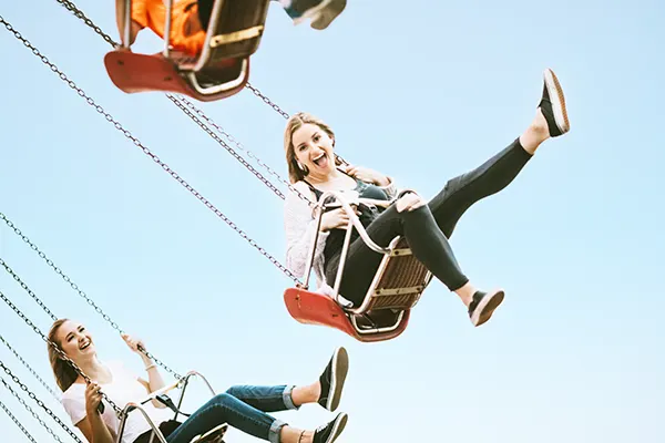 People enjoying a carnival swing ride against a blue sky, laughing with legs extended in mid-air.