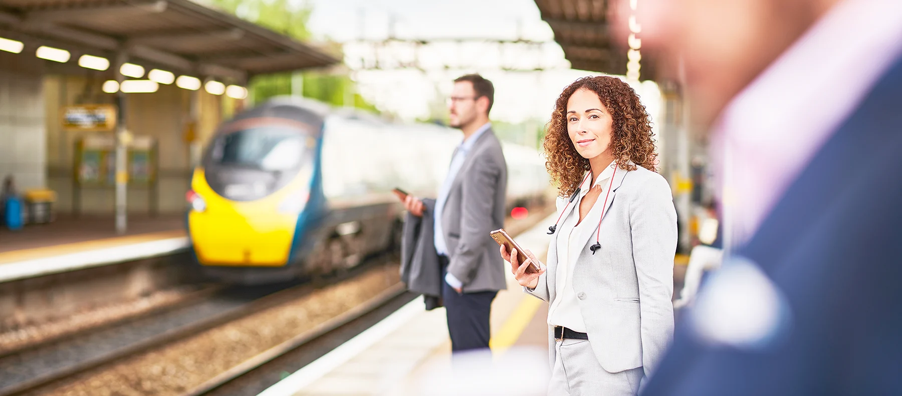 Business travellers standing on a railway platform holding mobile phones, a train is pulling into the opposite platform.