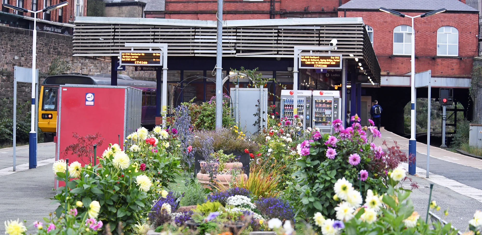 A station platform with a large planter full of a variety of colourful flowers. 