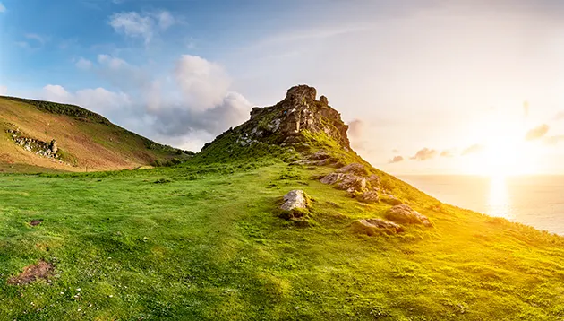 A grass covered rocky clifftop overlooking the sea at sunset. 