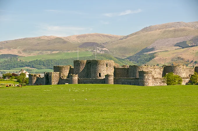 The ruins of an ancient castle in a green field with hills in the background and a blue sky above. 