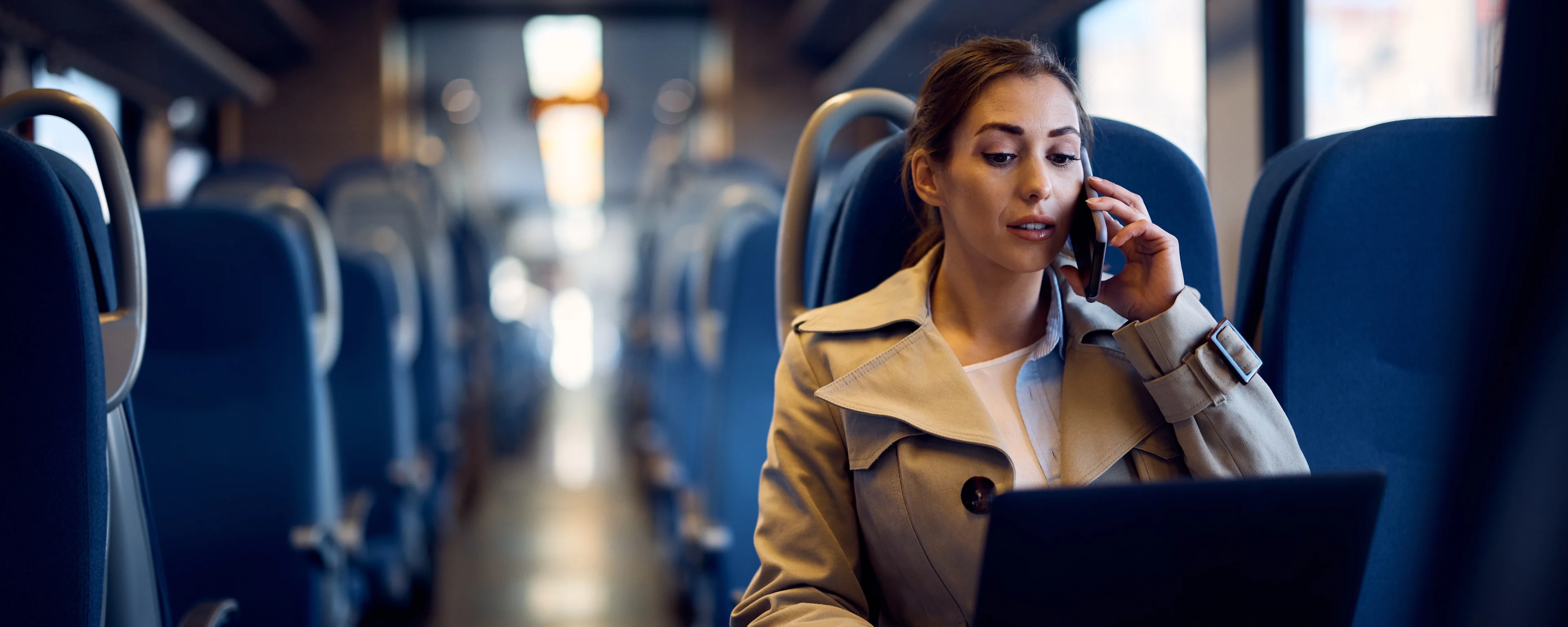A young woman talking on a phone and working on a laptop on the train