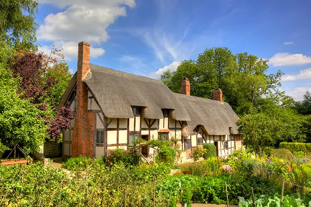 A thatched cottage set in a lush garden with a blue sky behind. 