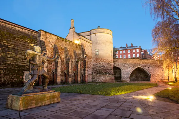 A stone castle at twilight, with a statue of a man with a bow and arrow to the left. 