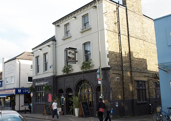 Exterior of a 3-storey brick pub on a busy street on a sunny day. 