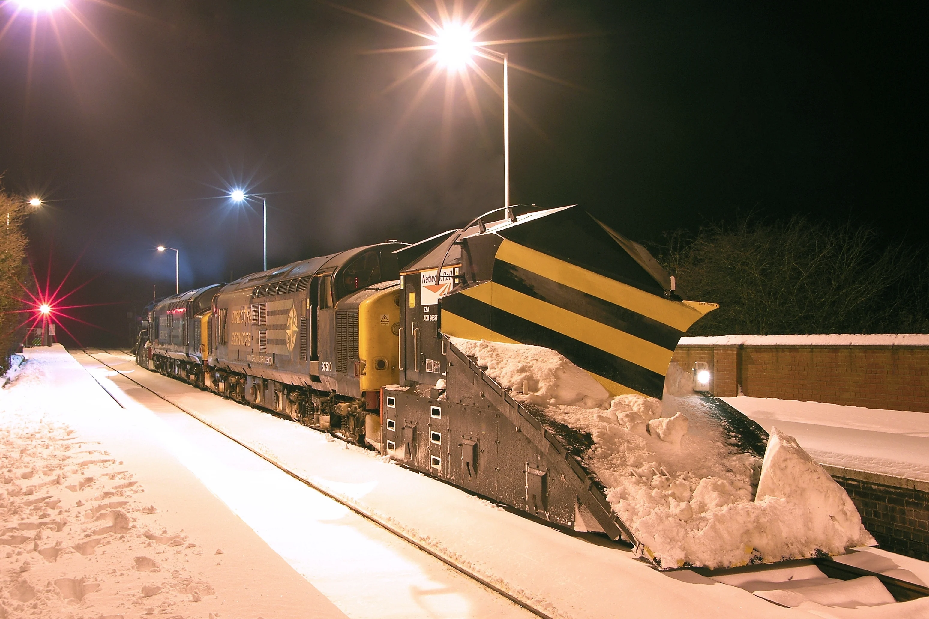 A snowplough clearing a railway track at night.