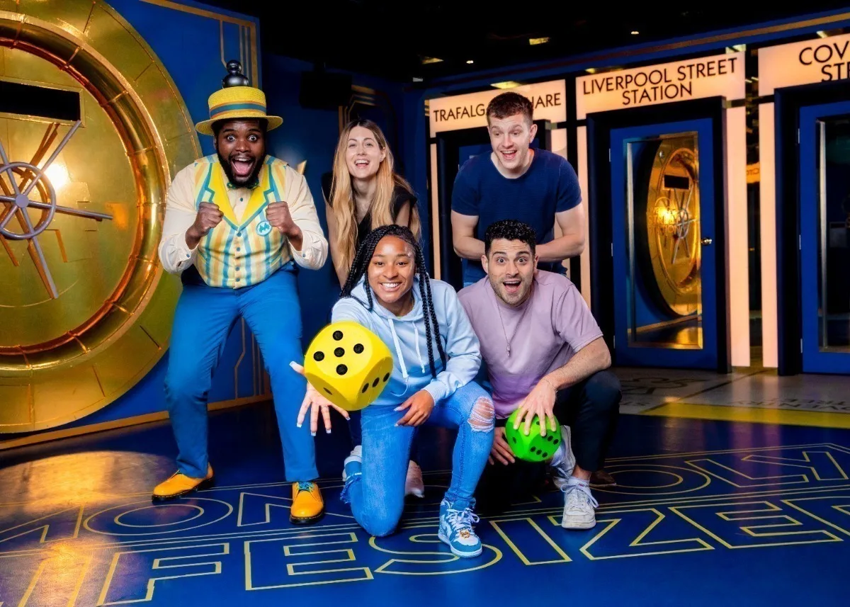 A group of people rolling a giant dice and playing a life-sized game of Monopoly. 