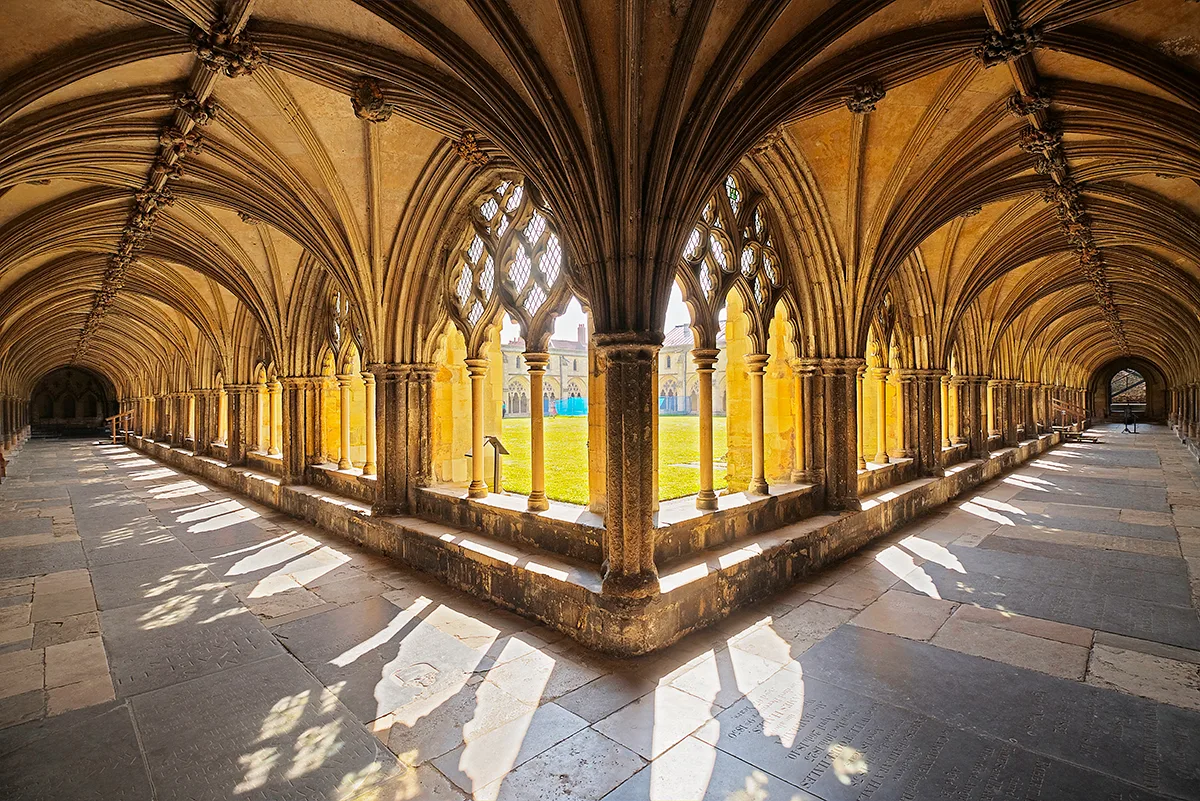 The cloister of a cathedral: stone corridors with open arches onto a quadrangle of grass. 