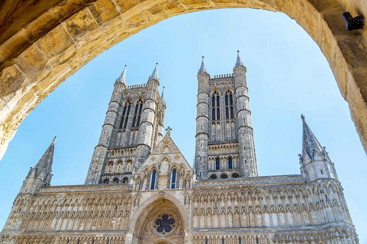 Looking up at a huge stone cathedral against a bright blue sky, with the view framed by a stone archway. 