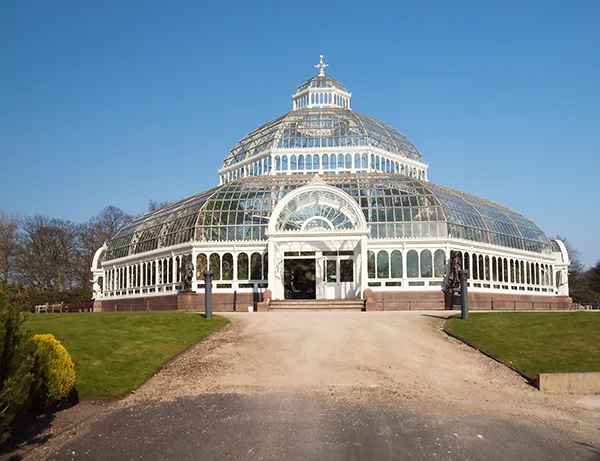 A large domed greenhouse in a park, against a blue sky. 