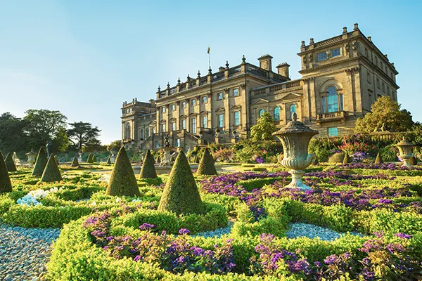 A large stately home with a lavish ornamental garden in front. 
