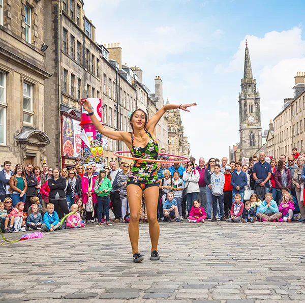 A young woman in a swimming costume hula hooping on a city street in front of a large crowd.