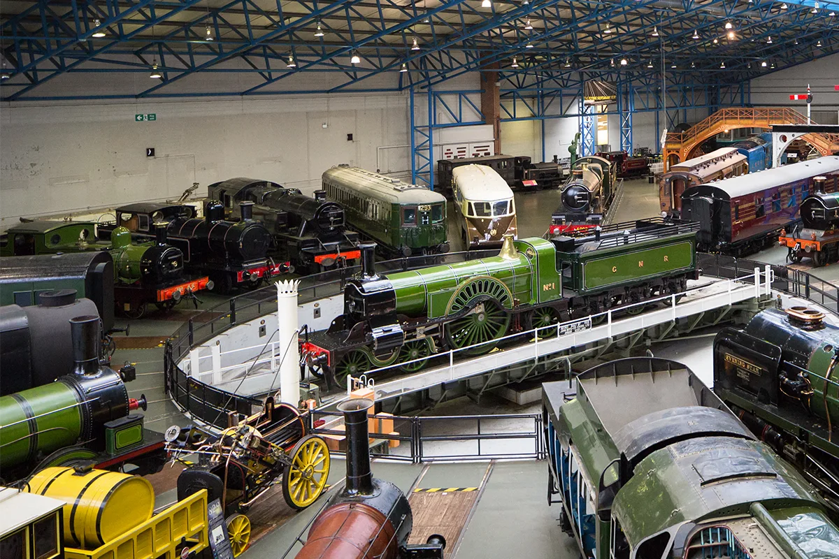 A locomotive on a turntable surrounded by other vintage trains and coaches at the National Railway Museum