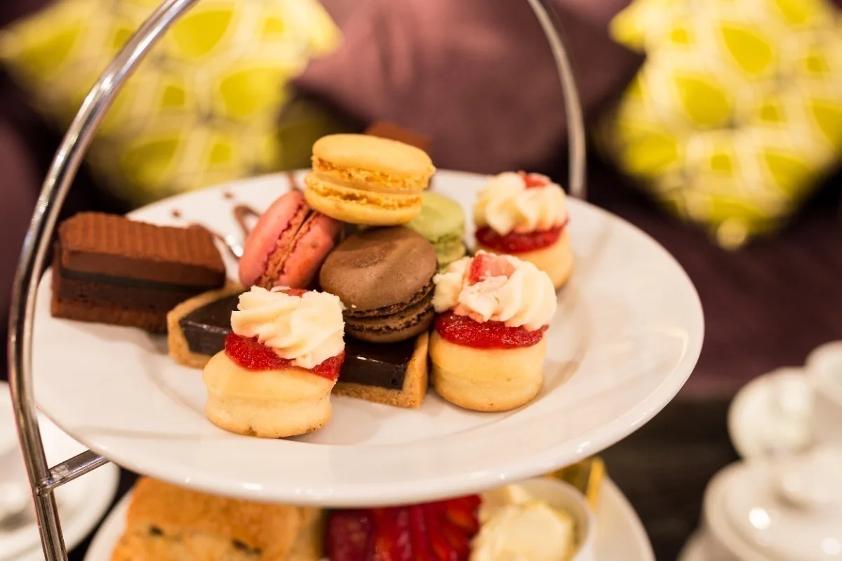 An assortment of small cakes on layered white plates, ready for afternoon tea. 