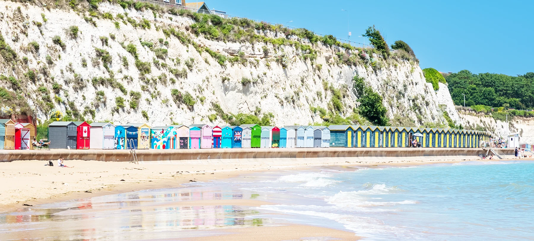 A row of colourful beach huts in Broadstairs, Kent, with the sea in the foreground and cliffs behind.