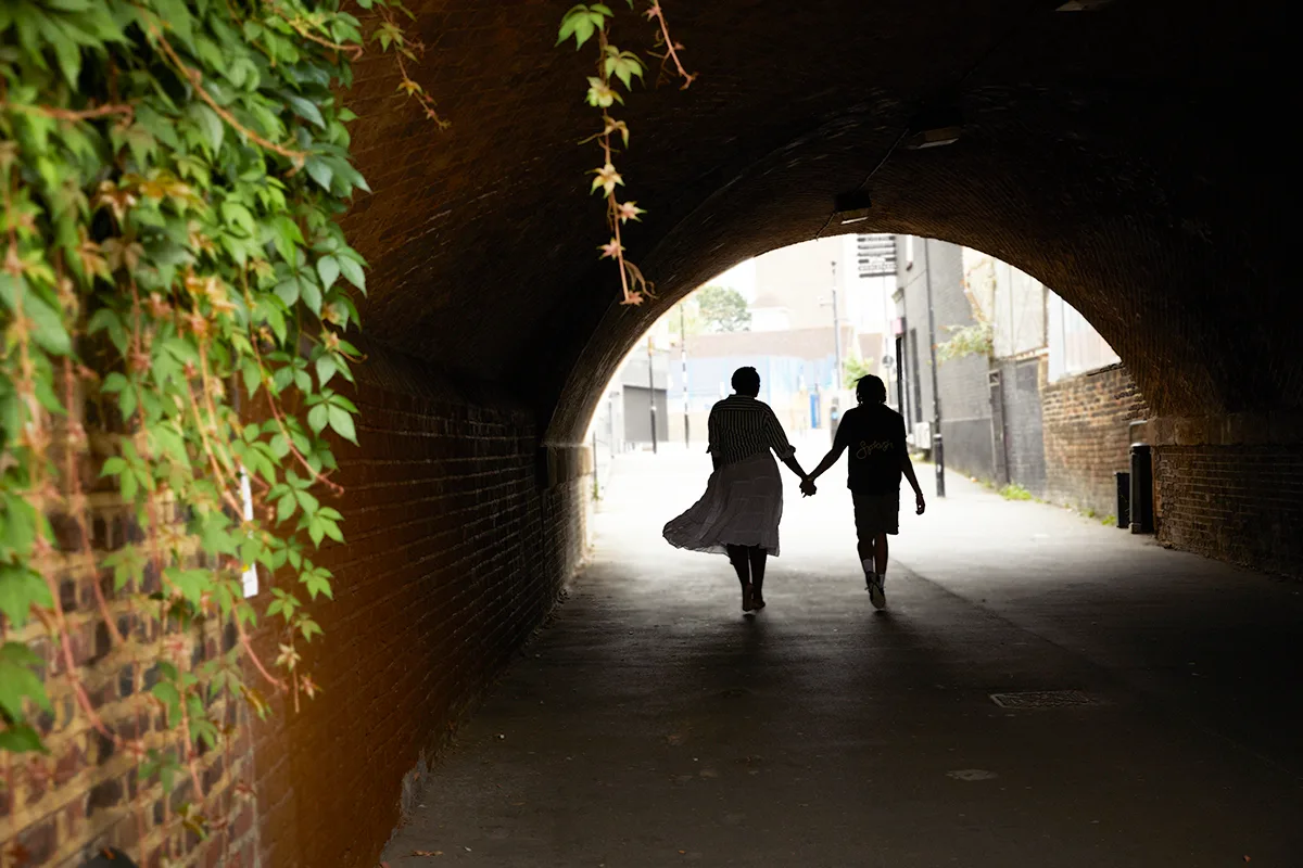 A couple in silhouette holding hands and walking through a tunnel.