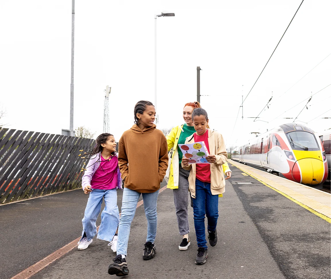 A family walking along a train platform with a modern red and yellow train visible in the background.