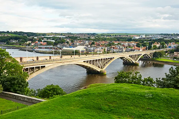 A bridge across a wide river with a picturesque village on the other side. 