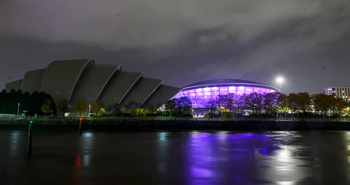 Glasgow's SEC Armadillo and Hydro arenas illuminated at night with purple lights reflecting on the River Clyde.