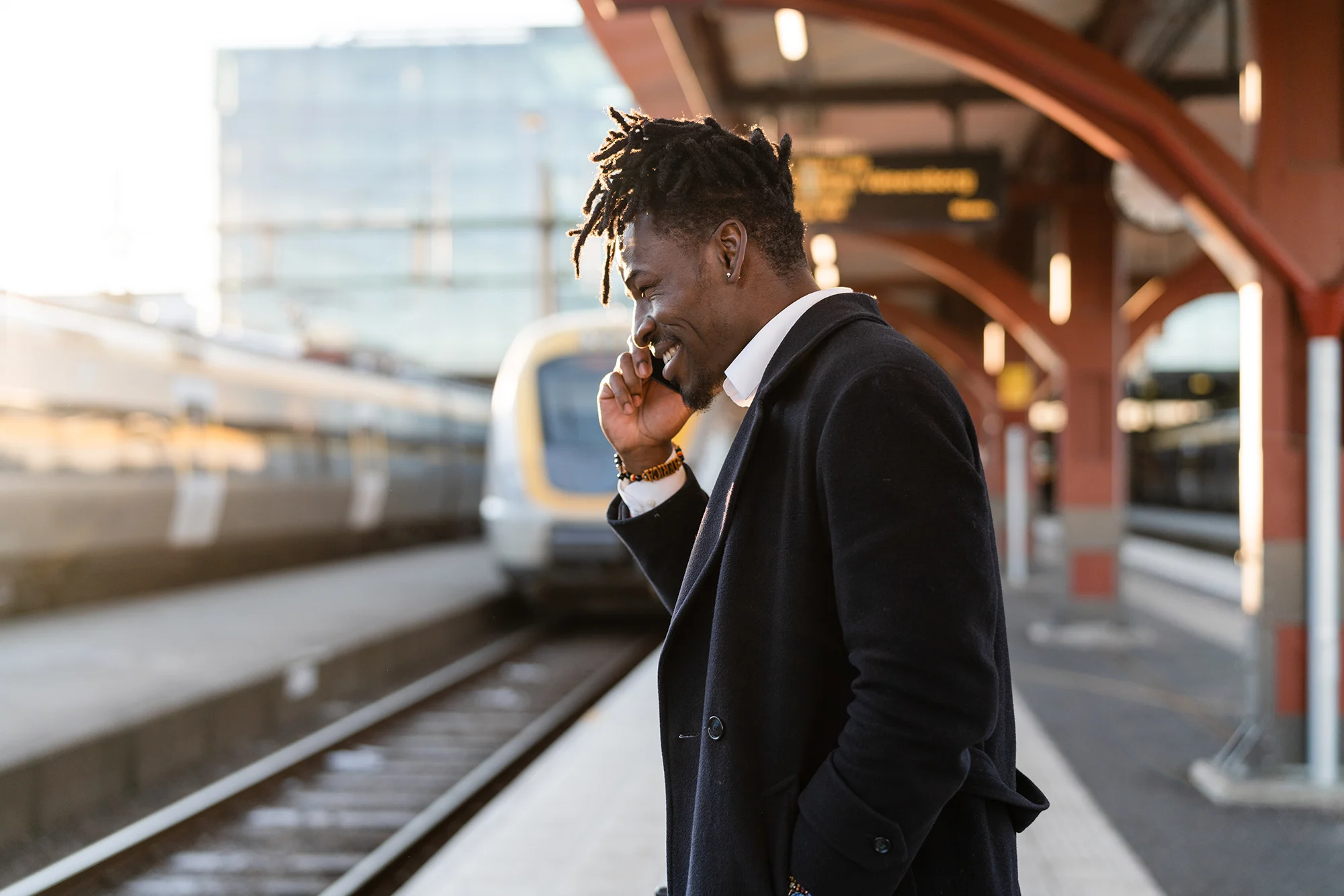 A businessman talks on the phone at a railway station while waiting for a train to pull into the platform