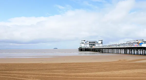 A sandy beach with the tide out and a long pier jutting out to sea. 