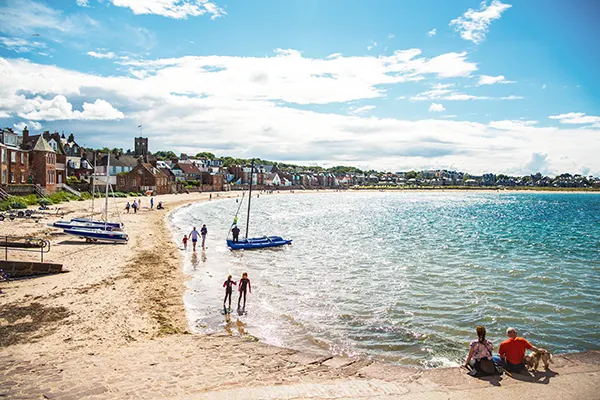 A sandy horseshoe beach with blue water and red brick houses set back from the beach edge. 