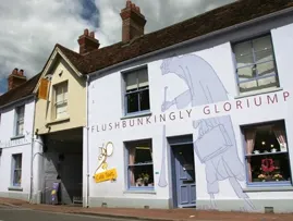Exterior of the 2-storey building of the Roald Dahl Museum, painted light blue with the words "flushbunkingly gloriumptious: across it.