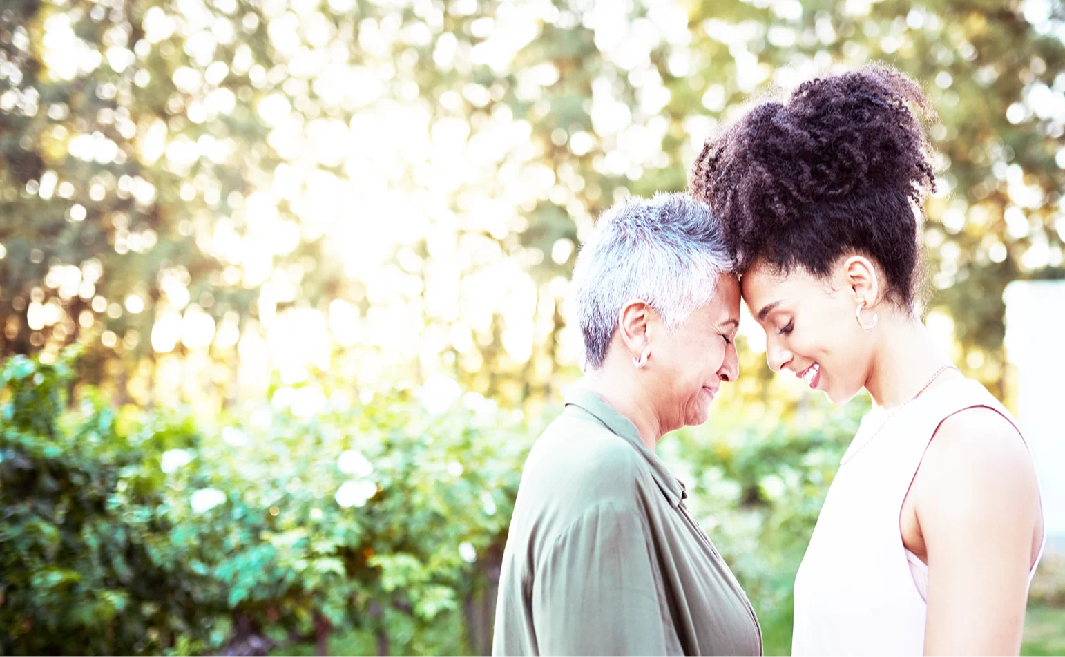 A Black woman with short grey hair smiling and being embraced by a younger smiling Black woman.