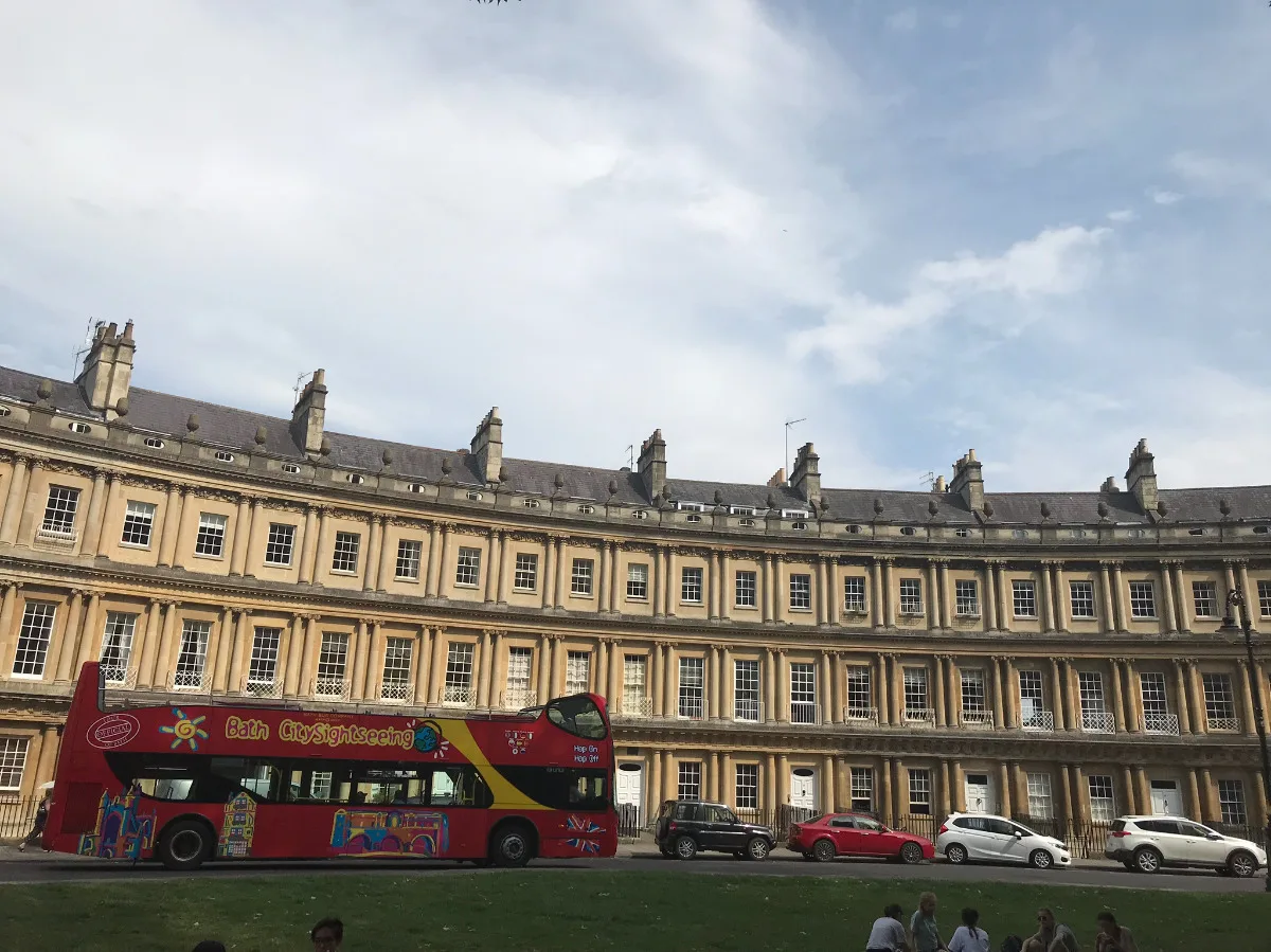 A red Bath City Sightseeing open-top bus passes the curved Georgian architecture of the Royal Crescent in Bath.