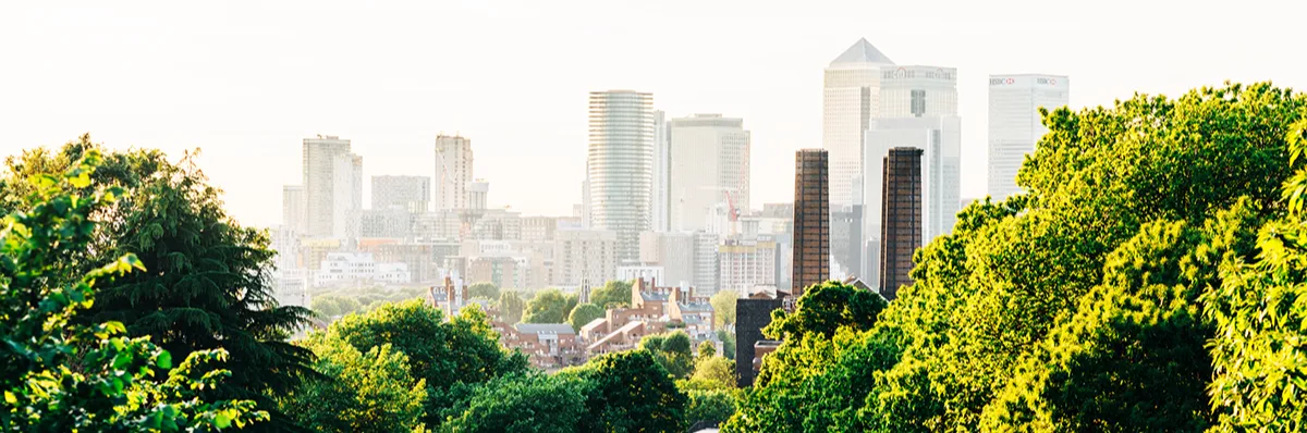 A London park with trees on every side, with a view towards the tall buildings of the City. 