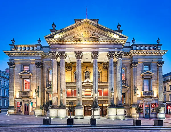 A grand theatre with columns at the front illuminated at dusk.
