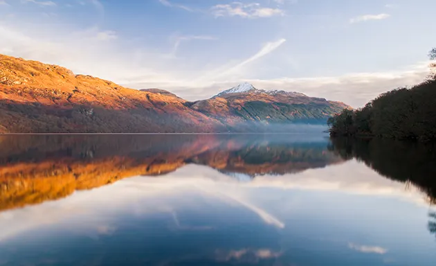 The hills of the Scottish highlands reflected in the still water of a loch.
