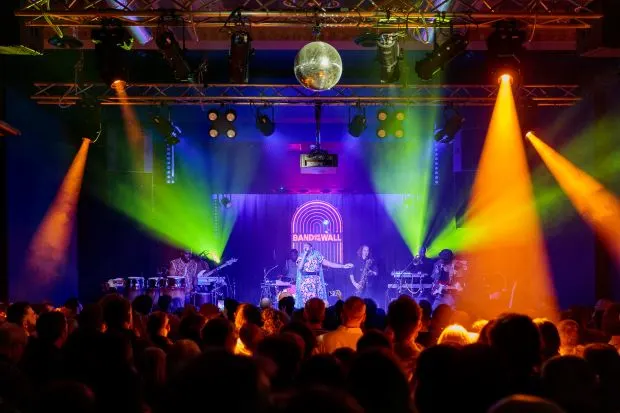 People dancing in a colourfully lit up room with disco ball and person singing on stage