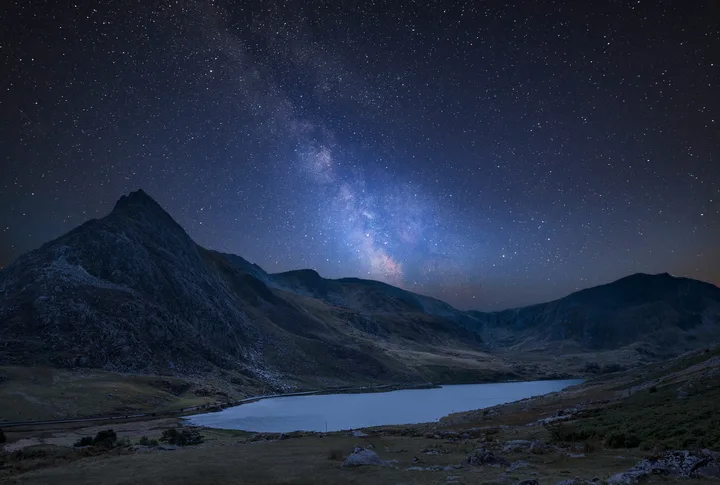 A clear night sky sparkling with stars over a still lake and mountains. 