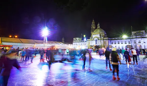 Ice skaters on an open-air city centre rink at night.