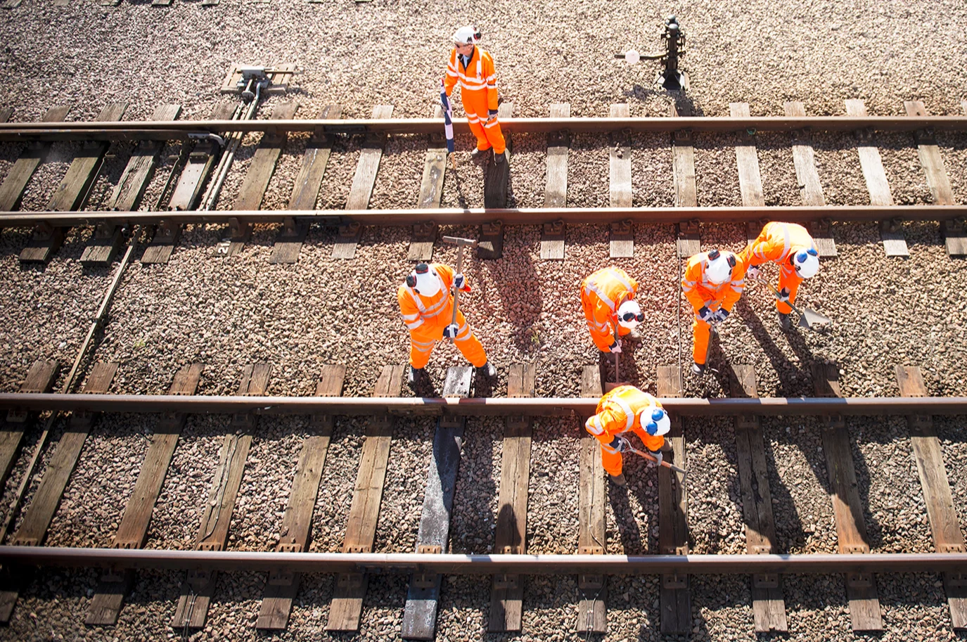6 workers in orange jumpsuits and white hardhats working on a train track in the daytime.