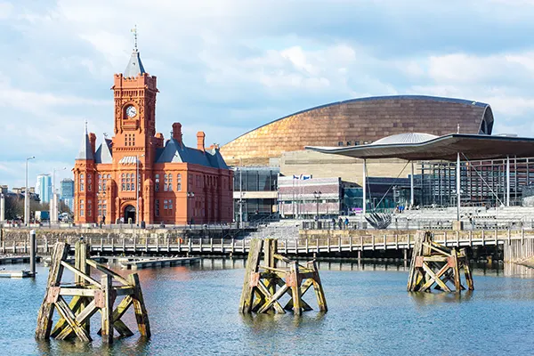 An industrial harbour with a red brick church with a grey spire in front of a large modern curved building with a metallic tiled finish.