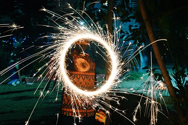 A man in traditional Indian dress swirling a sparkler to create a bright circle. 