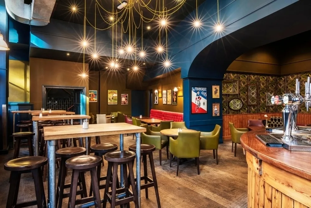 The interior of a bistro with wooden floors, dark blue walls and a range of tables and booths. 