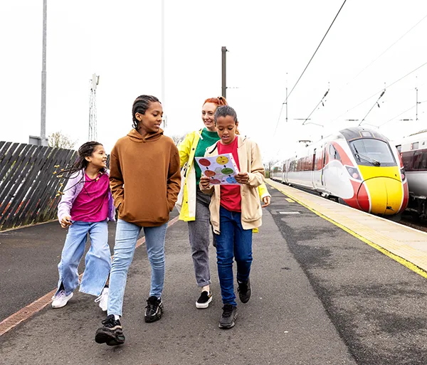 A family walking along a train platform with a modern red and yellow train visible in the background.