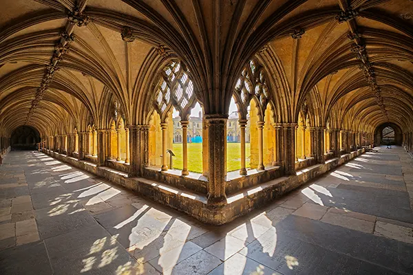 The cloister of a cathedral: stone corridors with open arches onto a quadrangle of grass. 