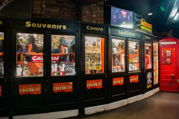 Windows of The Cavern Club memorabilia surrounded by black walls with a sign saying 'Souvenirs'. Red Telephone Box on right of image.