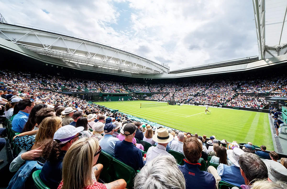 Packed Centre Court at Wimbledon tennis tournament with spectators watching a match on the pristine grass court.